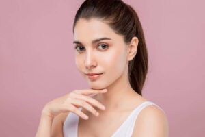 Woman with smooth, symmetrical nose and confident expression after cleft rhinoplasty on a soft pink background.