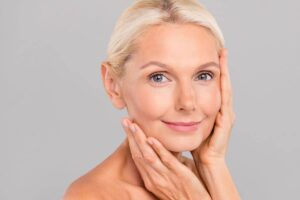 Middle-aged woman with glowing skin gently touching her face, showing facelift recovery progress and youthful results.