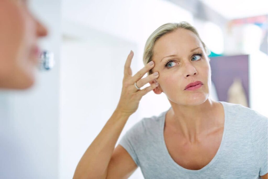 Concerned woman examining face in mirror, highlighting importance of recovery tips for facelift healing process