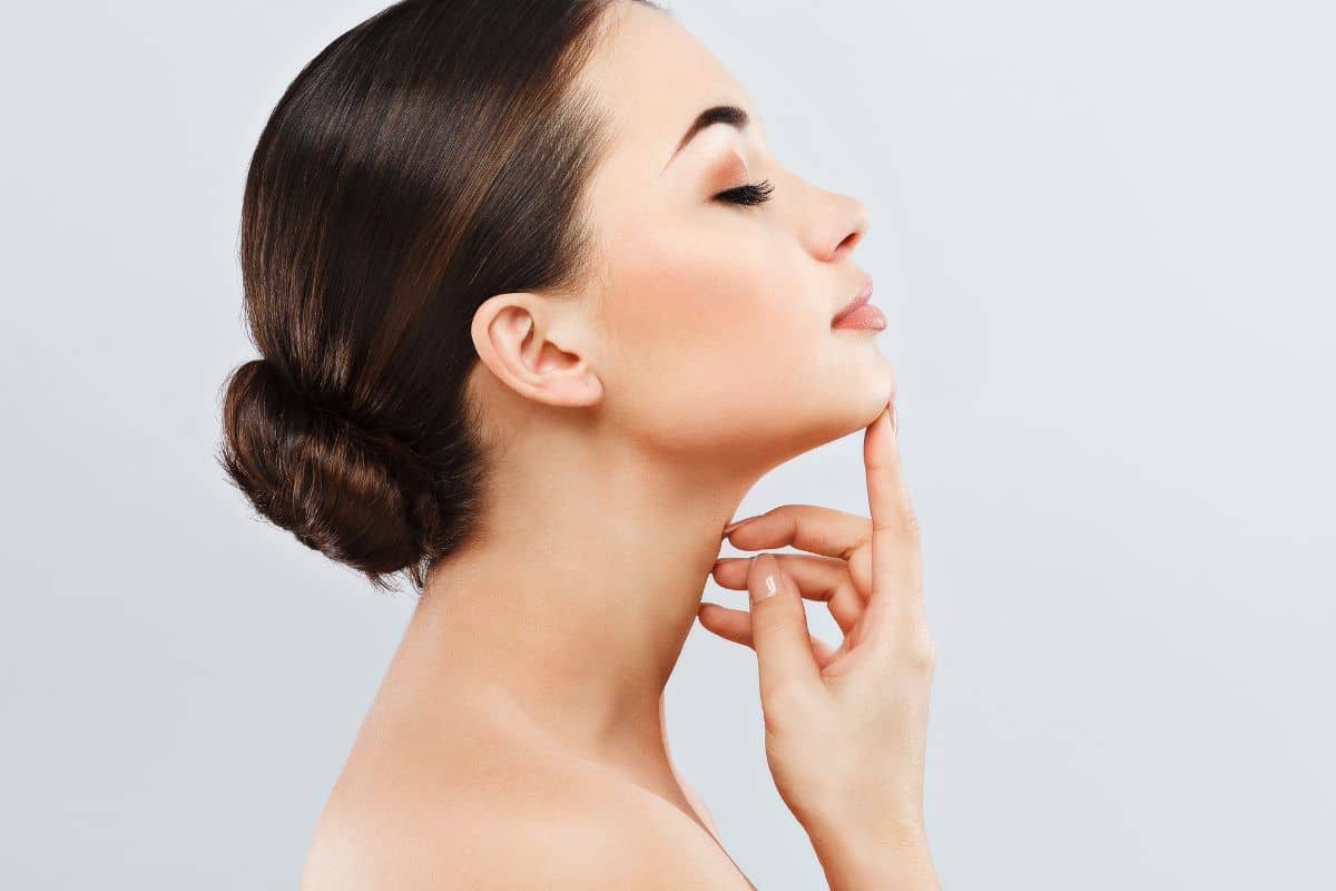 Woman touching her chin, showcasing refined nose profile relevant to open vs closed rhinoplasty comparison.