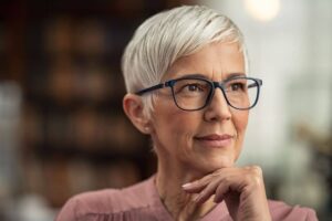 Elderly woman with short white hair and glasses reflecting calmly, representing facial skin cancer reconstruction concerns.