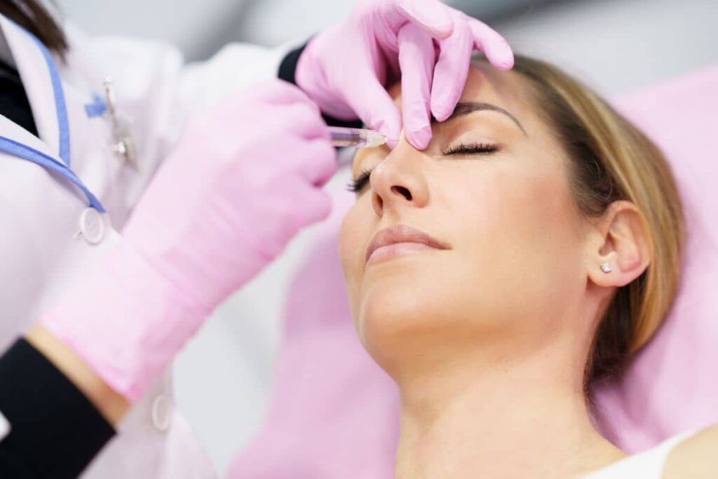 Doctor injecting hyaluronic acid filler into patient's nasal bridge during a liquid rhinoplasty procedure.