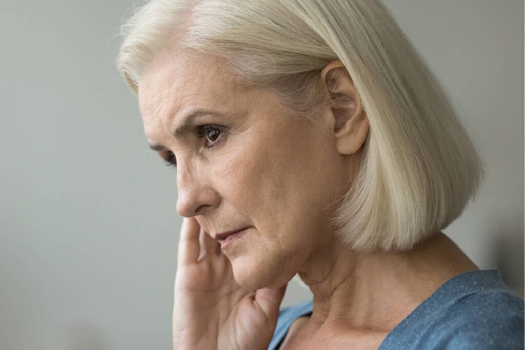 A side profile of a blonde woman looking thoughtfully into the distance while resting her hand near her jawline.